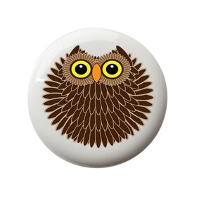 May include: A brown owl with yellow eyes and an orange beak. The owl is surrounded by brown feathers.