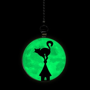 May include: A black cat silhouette perched on a house roof against a glowing green moon pendant.