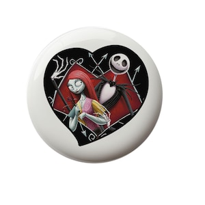 May include: A white ceramic ornament with a black heart-shaped design featuring Jack Skellington and Sally from The Nightmare Before Christmas. The heart is red with black accents and the characters are depicted in a romantic pose.
