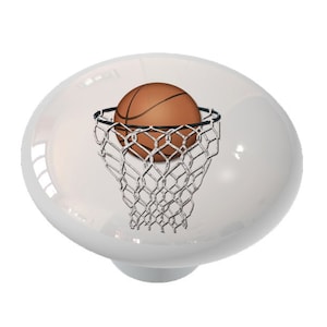 May include: A white ceramic knob with a basketball going through a net. The basketball is orange and brown with black lines. The net is black and white.