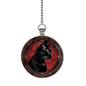 May include: A black cat with green eyes is featured on a round, silver light pull. The cat is set against a red background with a decorative, ornate border.