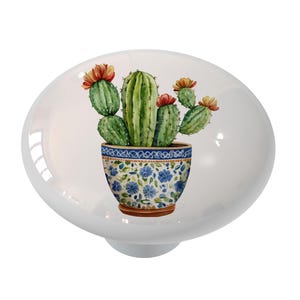 May include: A ceramic knob with a watercolor illustration of a cactus plant in a blue and white patterned pot with orange and red flowers.