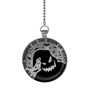 May include: A silver chain with a round pendant featuring a black silhouette of a character with the text "I am the shadow on the moon at night."