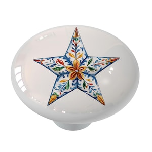 May include: A white ceramic knob with a blue, yellow, red, and green star design. The star has a floral pattern.