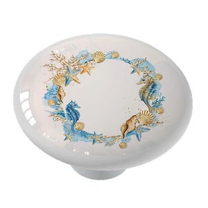 May include: White ceramic knob with a blue and gold watercolor design of seashells and seahorses. The design is in a circular wreath pattern.