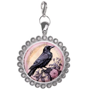 May include: A silver charm with a black crow perched on a branch of pink roses. The charm is surrounded by a circle of clear rhinestones.