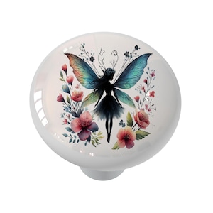 May include: White ceramic cabinet knob featuring a colorful fairy design. The fairy has iridescent wings and is surrounded by pink and red flowers. The knob is round with a glossy finish.