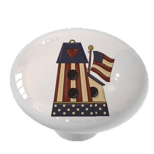 May include: A ceramic knob with a patriotic design featuring a red, white, and blue birdhouse with a heart on the front and an American flag on top.