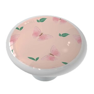 May include: A pink ceramic knob with a delicate butterfly and leaf pattern. The knob is round and has a white rim.