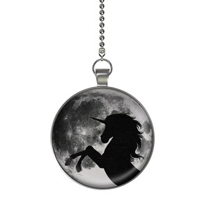 May include: A silver chain with a round pendant featuring a black silhouette of a unicorn against a moon-like background.