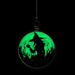 May include: A black silhouette of a witch holding a cauldron in front of a green moon. The witch is wearing a pointed hat and a long dress. The moon is surrounded by trees.