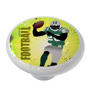 May include: A white ceramic knob with a green and yellow design featuring a silhouette of an American football player throwing a football. The text "AMERICAN FOOTBALL" is written in brown on the knob.