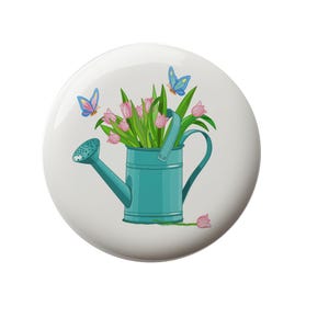 May include: A blue watering can with a bouquet of pink tulips and two blue butterflies. The watering can is on a white background.