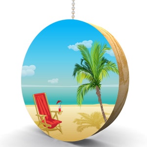 May include: A round wooden ornament with a beach scene. The scene features a red beach chair, a palm tree, and a blue ocean with white clouds in the sky.