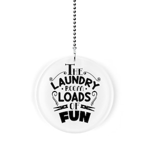 May include: A white round acrylic ornament with a black design that says "The Laundry Room Loads of Fun" with two clothespins on either side of the word "of". The ornament is hanging from a silver chain.