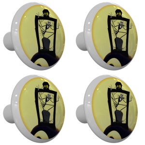 May include: Four white cabinet knobs with a Halloween-themed design. Each knob features a circular image of a skeleton in a graveyard scene with a full moon in the background. The knobs are likely for furniture.