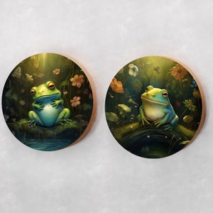May include: Two round wooden coasters with a green frog sitting on a mossy log in a forest setting. The frogs are surrounded by flowers and greenery. The coasters are perfect for adding a touch of nature to your home decor.