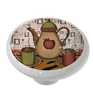 May include: A white ceramic knob with a colorful illustration of a teapot, two mugs, and a checkered pattern. The teapot has a red apple on the side and the mugs have steam coming out of them. The background is a brown and white pattern with the words "Coffee", "Tea", and "Scones".