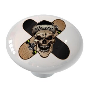 May include: A white ceramic knob with a graphic of a skull wearing a baseball cap that says "Skate" and two crossed skateboards.