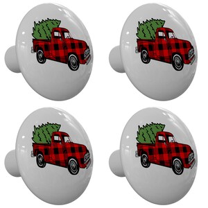May include: Four white cabinet knobs with a red and black buffalo plaid truck carrying a green Christmas tree. The knobs have a smooth, glossy finish and a silver-colored stem.