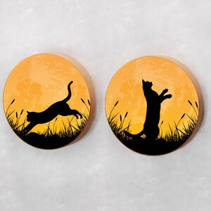 May include: Two round wooden wall decor pieces with a sunset orange background and black silhouette images of cats. One cat is jumping and the other is standing on its hind legs.