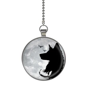 May include: A silver chain with a round pendant featuring a black silhouette of a wolf howling at the moon. The moon is depicted as a gray and white orb with a textured surface.