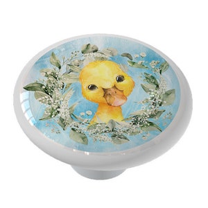 May include: A ceramic knob with a watercolor illustration of a yellow duckling with a blue background and white flowers.