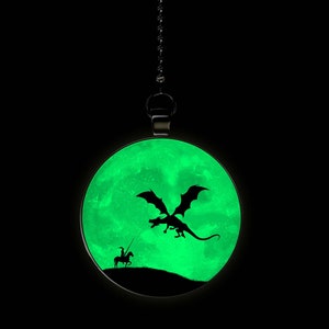 May include: A glow-in-the-dark pendant featuring a silhouette of a knight on horseback facing a dragon against a green moon background.