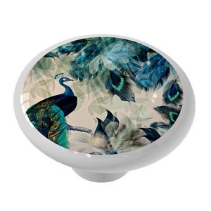 May include: A ceramic knob with a peacock design. The peacock is blue and green with a white background. The peacock is surrounded by feathers.