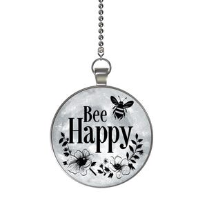 May include: A round, silver-toned pendant with the words "Bee Happy" in black script, accompanied by a bee illustration and floral accents. The pendant hangs from a silver chain, creating a cheerful and decorative accessory.