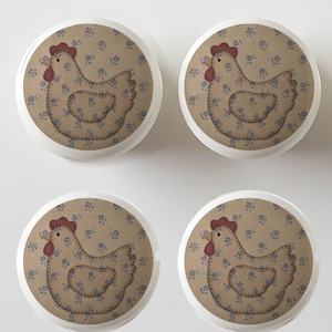 May include: Four white cabinet knobs with a circular design featuring a brown chicken silhouette on a beige background with blue floral patterns. The chicken has a red comb and wattle.
