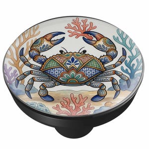 May include: A round cabinet knob featuring a colorful illustration of a crab with intricate geometric patterns on its shell. The crab is surrounded by coral reefs in shades of orange, blue, and purple against a sandy background on a black base.
