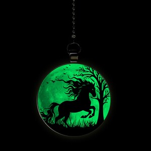 May include: A black silhouette of a horse running through a forest, set against a glowing green moon. The image is on a round pendant, hanging from a black chain.