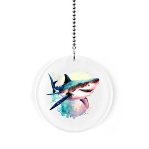 May include: A white ceiling fan pull chain with a round, clear acrylic charm featuring a watercolor illustration of a great white shark swimming in blue and green water.