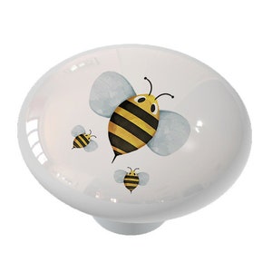 May include: White ceramic knob with a watercolor design of three bees. The bees are yellow and black with blue wings.