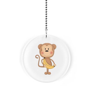May include: A round, clear acrylic ceiling fan pull with a cartoon monkey holding a banana. The monkey is brown with a yellow banana and has a smiling face.
