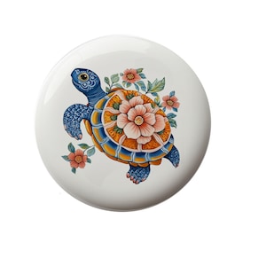 May include: A white ceramic plate with a hand-painted design of a blue and orange turtle with pink flowers.