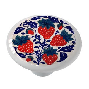 May include: White ceramic cabinet knob with a vibrant strawberry design. The knob features red strawberries with white seeds, blue-green leaves, and blue vines against a cream background. A decorative accent for furniture.