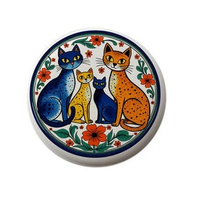 May include: A white ceramic plate with a blue, orange, and yellow cat design. The cats are surrounded by a floral border with red, orange, and green flowers.