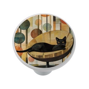 May include: A white cabinet knob featuring a black cat lounging in a mid-century modern chair. The cat has yellow eyes and a white whisker. The background has a retro design with colorful circles and vertical lines.