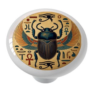 May include: White ceramic cabinet knob featuring an Egyptian scarab beetle design. The beetle is depicted with blue, gold, and red accents, surrounded by hieroglyphs and the Eye of Horus. A decorative accent for furniture.