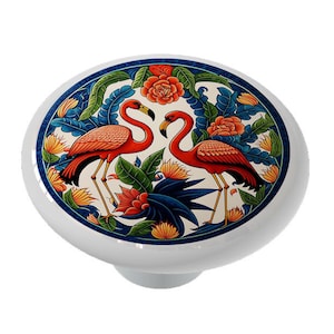 May include: A ceramic knob with a colorful design featuring two pink flamingos standing in a tropical garden with blue, green, and yellow flowers.