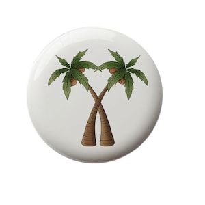 May include: A white ceramic tile with a hand-drawn illustration of two palm trees with brown trunks and green leaves. The trees are intertwined and have coconuts on them.