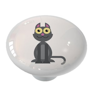 May include: A ceramic knob with a cartoon black cat with yellow eyes and pink ears. The cat is sitting with its tail curled around its legs.