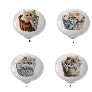 May include: Eight ceramic cabinet knobs with a white background and a colorful image of a cat in a basket. The cat is either white, gray, or brown and white. The basket is either wicker or woven.