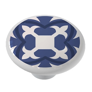 May include: A white ceramic knob with a blue and white geometric pattern. The pattern features a central square with four curved arms extending outwards.