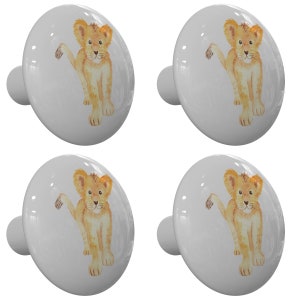 May include: Four white ceramic cabinet knobs. Each knob features a watercolor illustration of a light brown lion cub with a raised paw. The knobs have a glossy finish and a cylindrical base for mounting. Ideal for children's furniture or a safari-themed room.