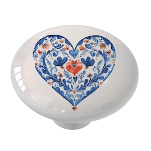 May include: White ceramic knob with a blue and red heart design. The heart is filled with intricate floral patterns.