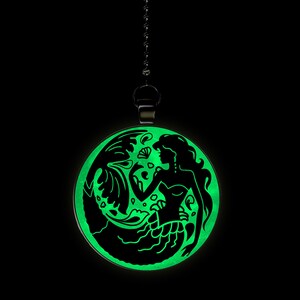 May include: A glow-in-the-dark pendant featuring a black silhouette of a mermaid with flowing hair and a tail. The pendant is round and hangs from a black chain.