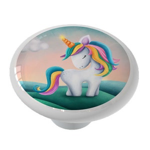 May include: A ceramic knob with a colorful illustration of a unicorn with a rainbow mane and tail standing on a green hill. The background is a pink and orange sunset.